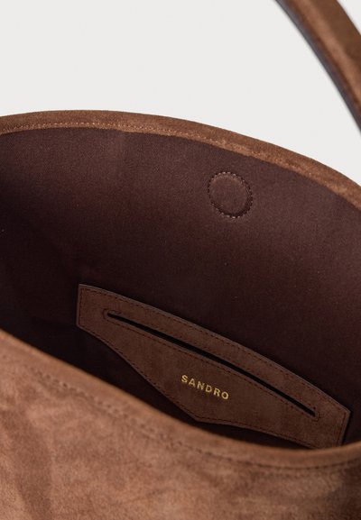 Intérieur d'un sac à main en daim marron avec une petite poche étiquetée "SANDRO" en lettres dorées et une fermeture magnétique.