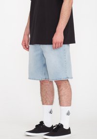 Hellblaue Jeansshorts mit geradem Schnitt und rohem Saum. Kombiniert mit einem schwarzen T-Shirt, schwarzen Sneakers und weißen Socken mit Logo.