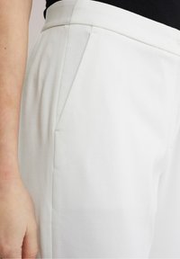 Bílé kalhoty ze směsového bavlněného materiálu s jemnou texturou, elastickým pasem a bočními kapsami, které mají dobře padnoucí střih a mírné sklady.