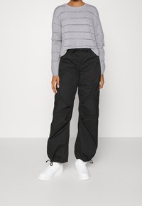Pull en tricot gris avec des rayures ajourées, associé à un pantalon cargo noir ample et des baskets blanches. Coupe décontractée et tissu léger.