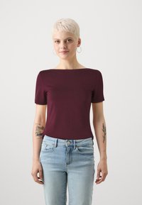 Burgunderfarget t-skjorte med korte ermer og båthals, laget av mykt stoff. Brukt sammen med lyseblå denimjeans. Enkelt design uten mønster.