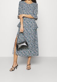 Blommönstrad klänning i blått och vitt med peplummidja, med en sidoklyvning; kombinerad med en svart texturerad handväska och svarta remsandaler.
