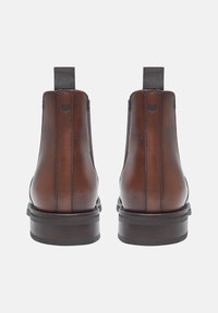 Bottines en cuir marron avec des panneaux élastiques sur les côtés, à bout rond et à talon plat. Présente des coutures subtiles et un petit détail de logo à l'arrière.