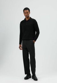 Zwarte gebreide polotrui met een kraag en drie knopen, gecombineerd met op maat gemaakte donkere broek en zwarte schoenen, wat zorgt voor een gestroomlijnde silhouet.