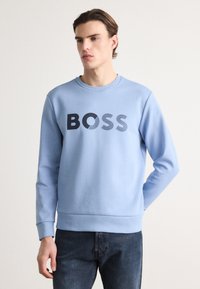 Light blue sweatshirt made of soft material, featuring a bold black "BOSS" logo in varying textures, with ribbed cuffs and hem.