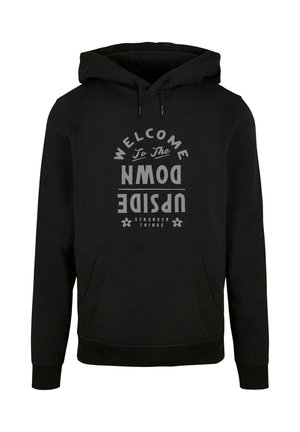 Melnas kapuces džemperis ar lielu pelēku grafiku tekstu "LAIPNI LŪDZAM UPSIDE DOWN" un "STRANGER THINGS" ar ziedu akcentiem, ar kangarū džepu.