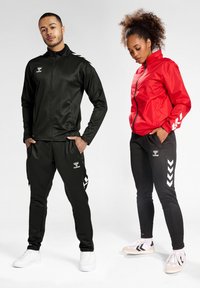 Svart atletisk jacka och byxor med vitt logotyp och chevrondesigner. R�öd zip-jacka parat med svarta byxor. Båda modellerna bär sportiga skor.