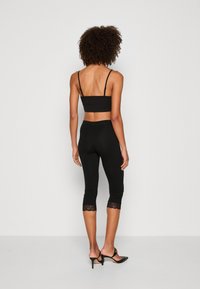 Sort crop top og leggings med blonder trim ved kanten. Leggingsene er beskåret midt på læggen. Stoffet ser blødt og tætsiddende ud.