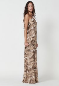 Maxi dress in a brown and beige fern pattern, made from lightweight fabric, featuring thin straps and a flowing silhouette.