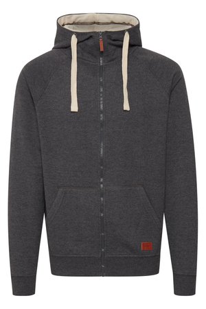 Sudadera con cremallera gris, confeccionada en tejido suave. Cuenta con una capucha forrada, cordones crema, bolsillos frontales y un pequeño parche de cuero con el logo en el dobladillo.