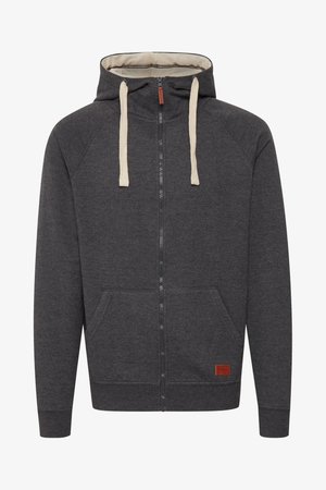 Gray zip-up hoodie made of soft fabric. Features a lined hood, cream drawstrings, front pockets, and a small leather logo patch on the hem.