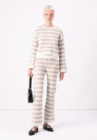 Ensemble en tricot deux pièces beige avec des rayures crème ; haut à manches longues court et pantalons évasés, doté d'une taille à cordon de serrage et d'un tissu texturé.