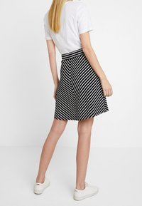 Jupe A-line noire et blanche à rayures, avec un motif en chevron, dotée d'une taille cintrée et d'un ourlet évasé. Portée avec un t-shirt blanc décontracté.