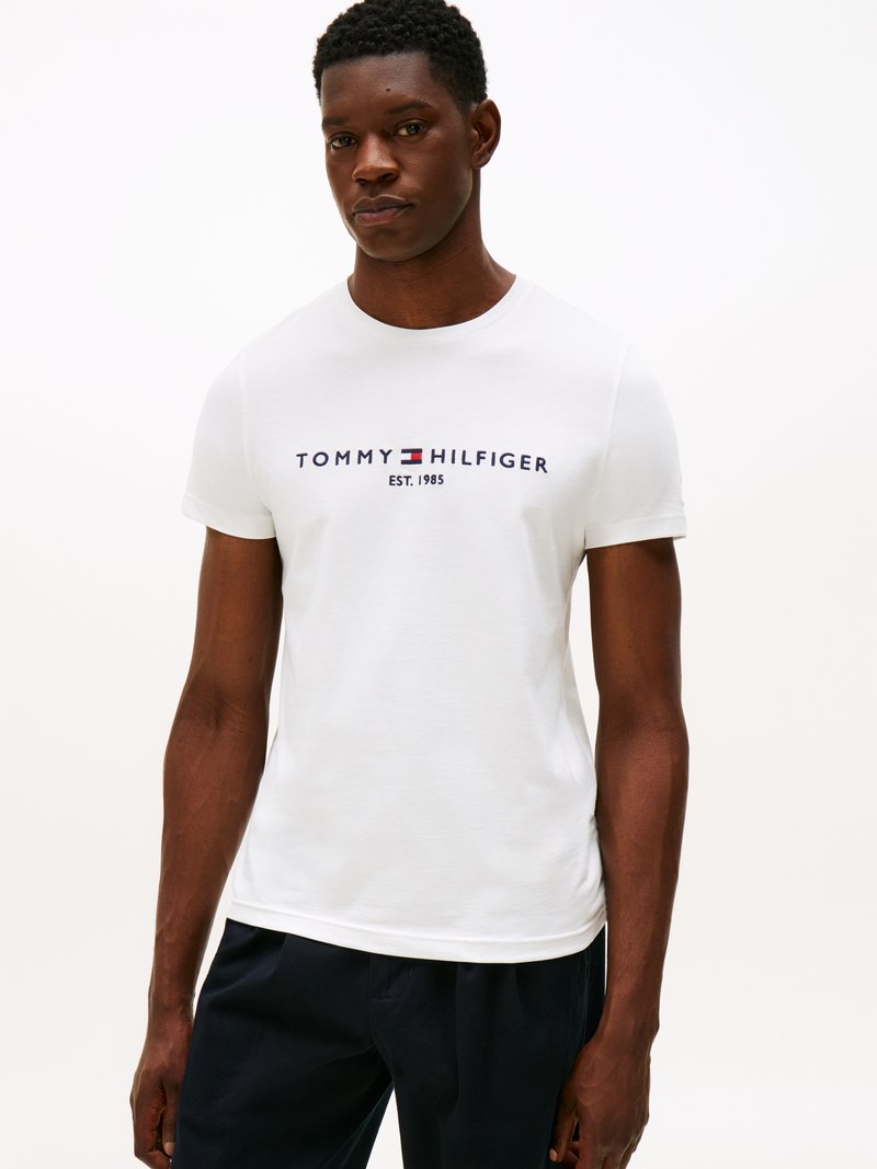 Λευκό κοντομάνικο T-shirt με στρογγυλή λαιμόκοψη, με το λογότυπο "TOMMY HILFIGER" σε ναυτικό μπλε, συμπληρωμένο με την αναφορά στον έτος ίδρυσης.