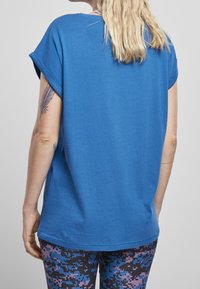 T-shirt di cotone blu con maniche corte arrotolate, caratterizzata da una vestibilità ampia. Indossata con leggings a fantasia nei colori blu, rosa e nero.