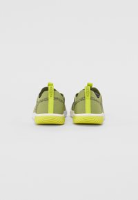 Grønne tekstilsneakers med et mønsterdesign, hvite såler og sterke gule detaljer, inkludert hælfliker og yttersåler.