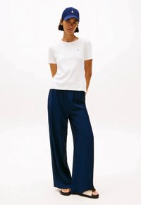 T-shirt branca de mangas curtas, calças largas azuis marinho, boné azul marinho e sandálias. Conjunto casual com um corte relaxado e minimalismo na marcação da camisola.