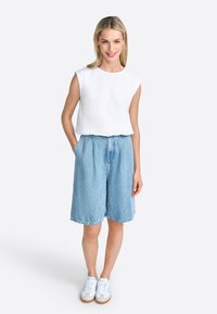 Top sin mangas blanco, pantalones cortos de mezclilla azul claros con bolsillos y zapatillas blancas. Tejido suave, corte relajado, diseño casual, dobladillos enrollados.