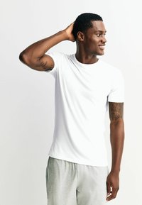 Balta īss piedurkņu T-krekls no mīksta auduma, pieguloša silueta un apaļas kakla līnijas, kombinēts ar gaiši pelēkām sporta biksēm.