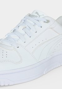 Κοντινό πλάνο λευκού sneaker Puma με λευκά κορδόνια, διάτρητες λεπτομέρειες και ραμμένες πινελιές στο δερμάτινο επάνω μέρος.