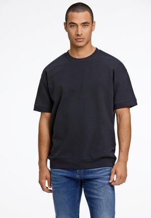 Sudadera de gran tamaño en azul marino con mangas cortas, cuello redondo y una textura suave. Combinada con jeans de denim ajustados.