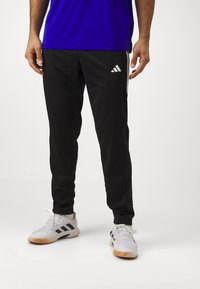 Svarta sportbyxor med smal passform, prydda med vit Adidas-logotyp och sidostraper, tillverkade av lätt och mjukt material.