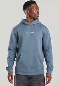 Light blue hoodie in soft fabric, featuring a kangaroo pocket and the text "Open Your Mind" in white. Ribbed cuffs and hem.