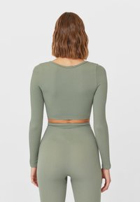 Top corto de manga larga acanalado en verde oliva. Presenta un escote redondeado y un diseño ajustado, combinado con bottoms de cintura alta a juego.