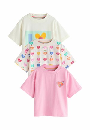 Smiling child with curly hair wearing a white shirt covered in colorful heart shapes spelling "LOVE" and blue jeans with a flower patch.