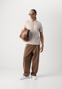 Beige polo-shirt med krage, brune løstsiddende bukser, hvide sneakers og en brun lædertaske. Tilbehøret inkluderer solbriller.