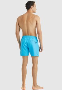 Modré plavky vyrobené z lehké tkaniny s elastickým pasem, zadní kapsou a elegantním designem. Žádné viditelné vzory ani akcenty.