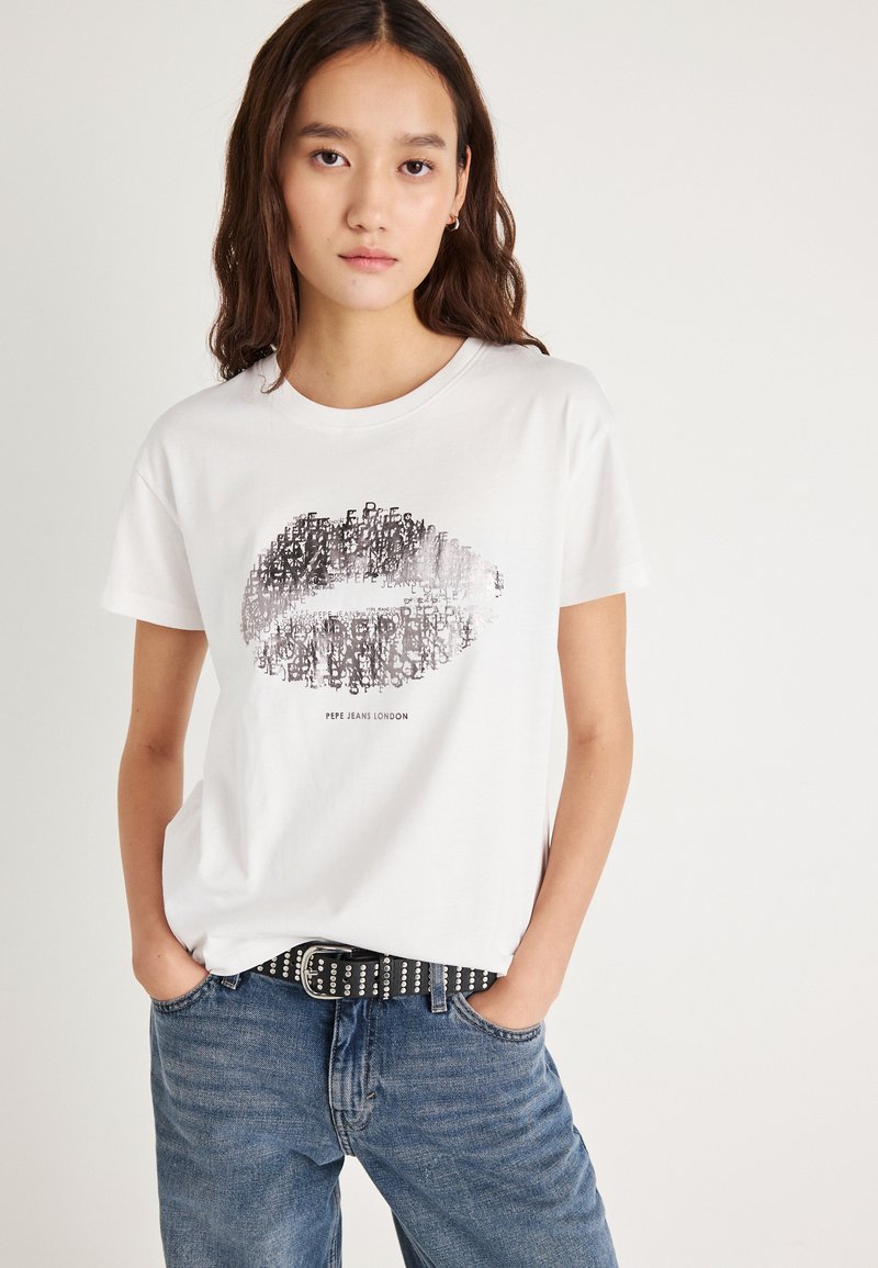 Hvit bomulls-t-skjorte med sort grafikk av lepper og tekst; ledig passform, korte ermer, kombinert med blå jeans og svart belte med nagler.