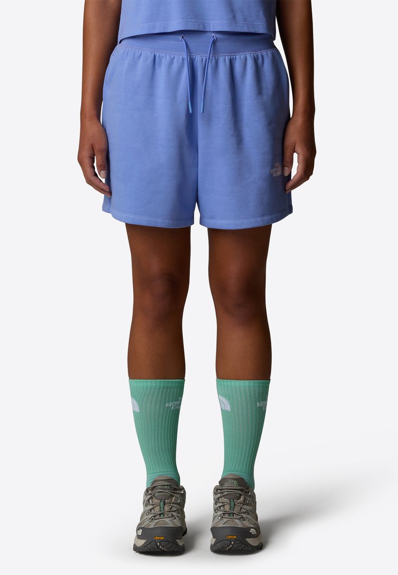 Himmelblaue Baumwollshorts mit elastischem Bund und Kordelzug. Kombiniert mit grünen Sportsocken und grauen Wanderschuhen mit strukturierten Sohlen.