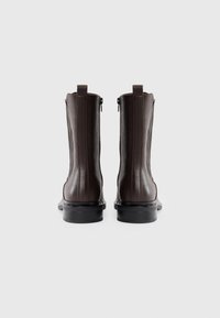 Brown leather ankle boots with a sleek design, side zippers, and ribbed detailing on the outer side. Black rubber soles provide durability.