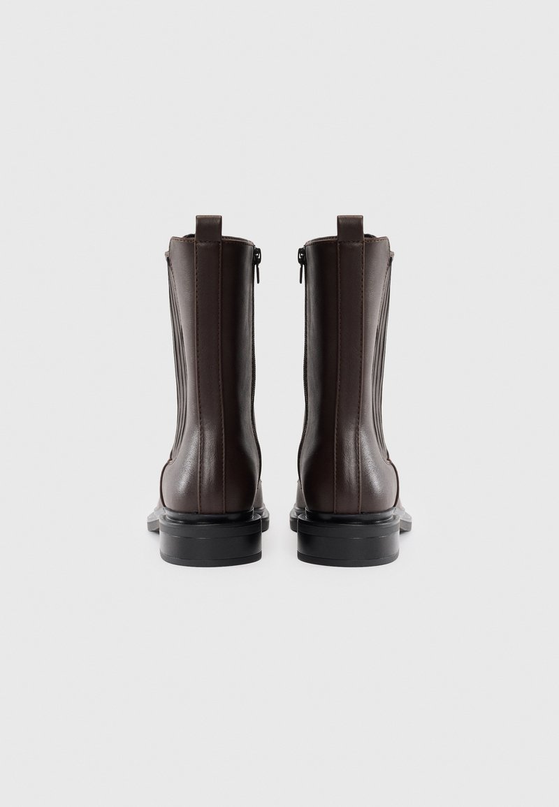 Stivali alla caviglia in pelle marrone con un design elegante, cerniere laterali e dettagli a coste sul lato esterno. Suole in gomma nera per una maggiore durata.