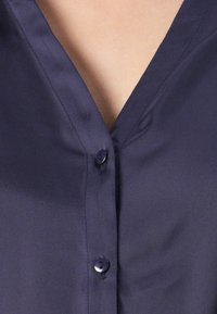 Close-up of dark blue buttoned shirt with two buttons fastened and V-shaped neckline showing skin.