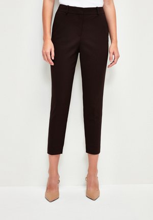Black slim-fit ankle-length trousers worn with beige pointed-toe heels and a white top, shown from waist to feet.