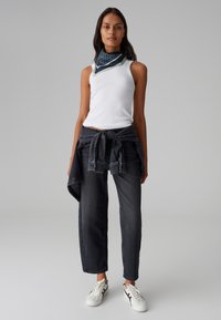 Canotta bianca a coste, jeans grigi scuri con giacca di jeans annodata in vita, sciarpa blu navy con pois bianchi e sneakers bianche con accenti neri.