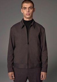 Dark brown zip-up jacket with a collared neckline, textured fabric, and side pockets. Paired with a matching pant.