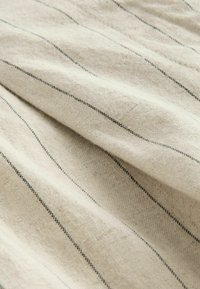 Hellbeige Stoff mit dünnen schwarzen Streifen, der eine weiche Textur und natürliche Faserdetails aufweist und ein zerknittertes, geschichtetes Aussehen zeigt.