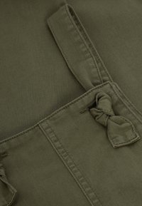 Gros plan sur un tissu vert olive avec des coutures détaillées et une sangle en tissu nouée attachée à une boucle.