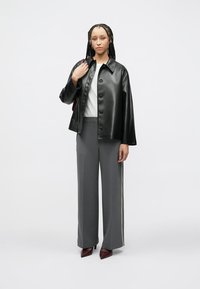 Μπουφάν από μαύρο δέρμα με κουμπιά, λευκό τοπ, γκρι παντελόνι με φαρδιά μπατζάκια και ρίγα στο πλάι, και μπορντό ψηλοτάκουνα. Ομαλή υφή με άνετη εφαρμογή.