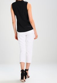 Zwarte mouwloze top, witte cropped broek en zwarte hoge hakken. Gladde stof, aansluitend ontwerp, en enkelbandjes op de schoenen.
