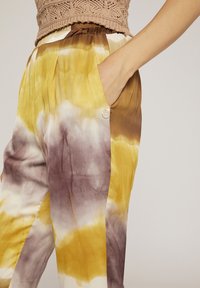 Lösa byxor i mjukt tyg med ett batikmönster i gult, brunt och vitt. Inkluderar sidfickor och en knappdetalj.