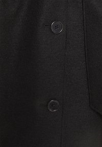 Cappotto di lana nera caratterizzato da una texture liscia, due bottoni neri rotondi e un design pulito senza motivi o accenti visibili.