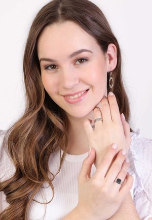 Silver drop earrings and a silver ring on a model’s hand. The model wears a light ribbed top with soft waves in her hair.