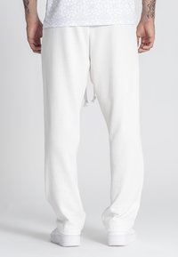 Pantalones de chándal blancos, texturizados, con un ajuste relajado y cordón ajustable en la cintura, que presentan puños ajustados y suaves.