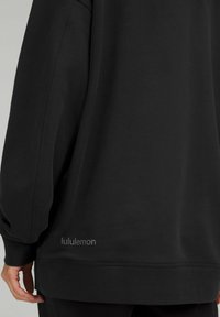 Felpa nera con collo a giro in morbido tessuto, caratterizzata da una vestibilità rilassata, orlo a costine e logo "lululemon" in una tonalità più chiara vicino al fondo.