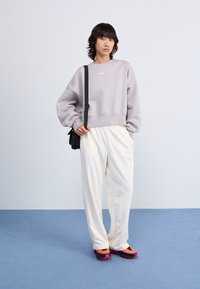 Grå oversized sweatshirt med en vit logotyp, krämfärgade vida byxor och flerfärgade sneakers med svarta, rosa och gula detaljer.