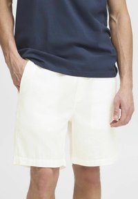 White textured shorts with a subtle pattern, featuring side pockets and a straight hem, paired with a navy blue t-shirt.